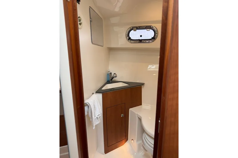 Slide: The Image of 2025 Pursuit OS 325 Offshore boat bathroom with wooden cabinetry and porthole window. - 68