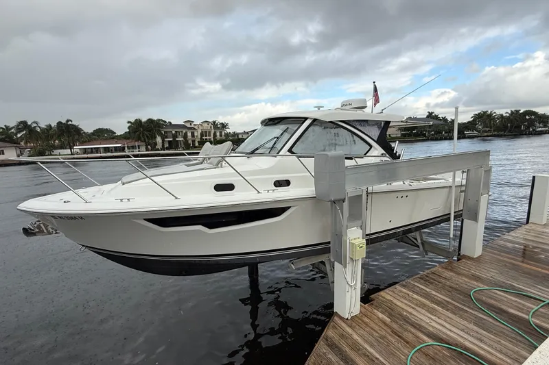 Slide: The Image of 2025 Pursuit OS 325 Offshore boat docked by waterfront homes under cloudy skies. - 96