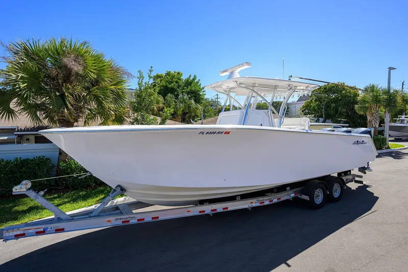 Slide: The Image of 2017 SeaHunter 33 Tournament boat on trailer, parked near palm trees under clear blue sky. - 2