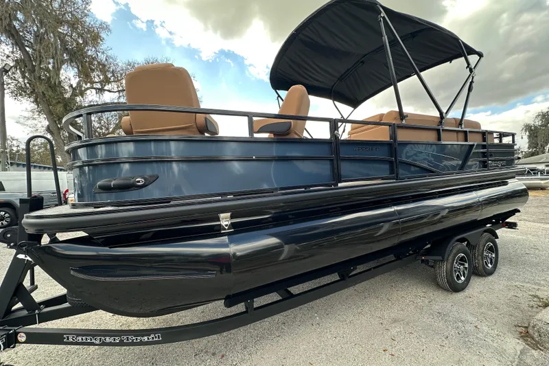 Slide: The Image of 2026 Ranger Reata 223FC pontoon boat with canopy on trailer, parked outdoors. - 2