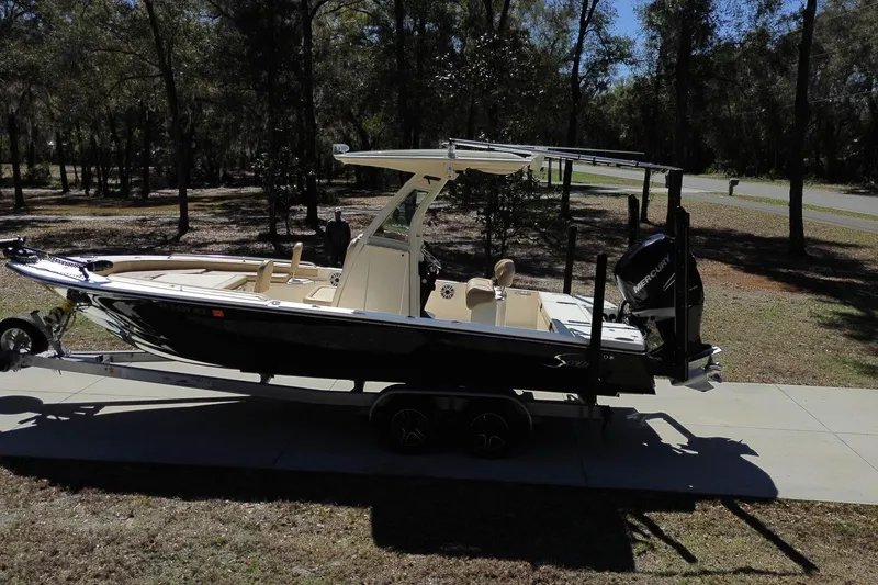 Slide: The Image of 2019 Scout 251 XSS boat parked on a driveway, surrounded by trees and grass. - 31