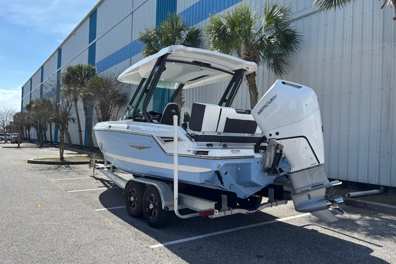 Slide: The Image of 2026 Monterey Elite 25 OB boat on trailer, parked near a building with palm trees. - 2