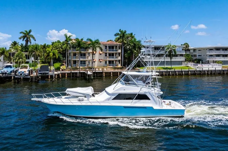 Slide: The Image of 1998 Bertram 60 Convertible yacht cruising near waterfront homes, under clear blue skies. - 5