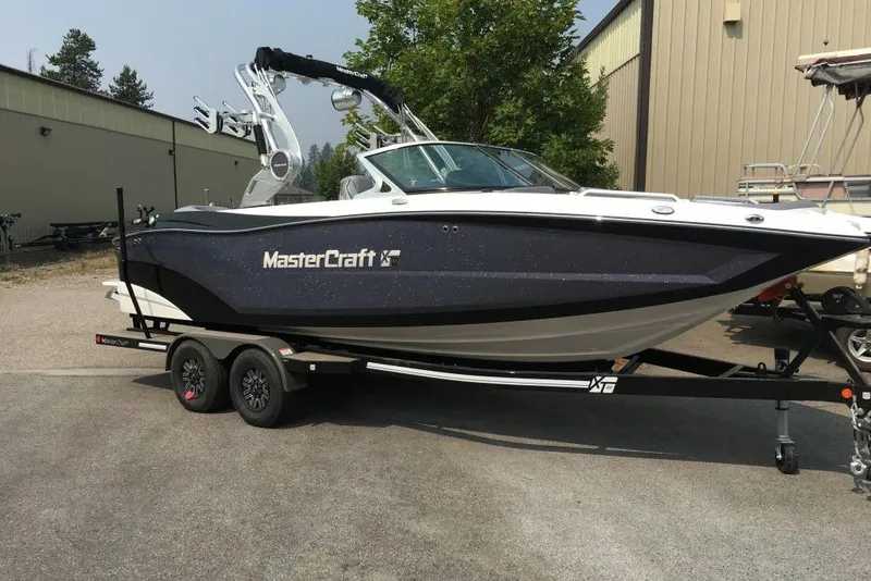 The Image of 2018 MasterCraft XT22 boat on trailer, parked outdoors near industrial buildings. - 0