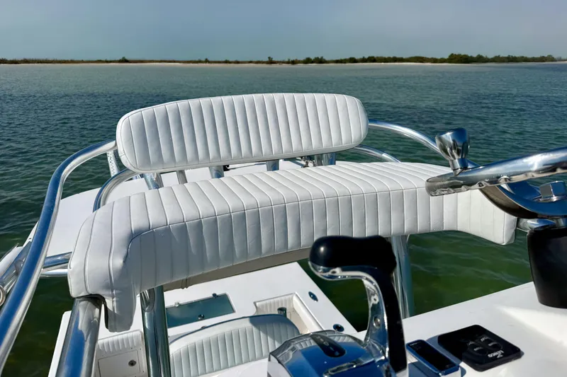Slide: The Image of 2019 Aquasport 244 Bay boat helm with white seating, steering wheel, and controls on calm water. - 25