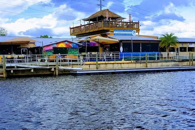 Slide: The Image of Waterfront building with colorful mural, palm tree, and outdoor seating under a blue sky. - 18