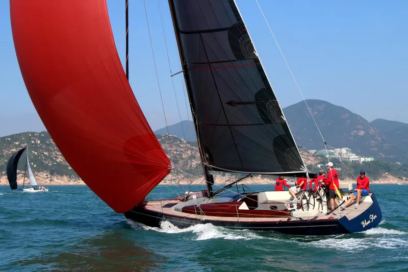 Slide: The Image of 2018 Tofinou 12 sailboat with red sail, crew onboard, sailing near scenic coastline. - 1