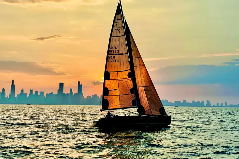 Slide: The Image of Sailboat Tofinou 12 (2018) on water at sunset with city skyline backdrop. - 3