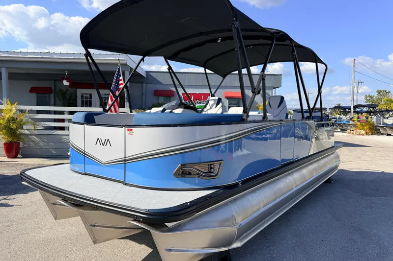 Slide: The Image of 2026 Avalon 2385 LSZ Quad Lounger Tri Toon boat, blue and silver, parked outdoors. - 2