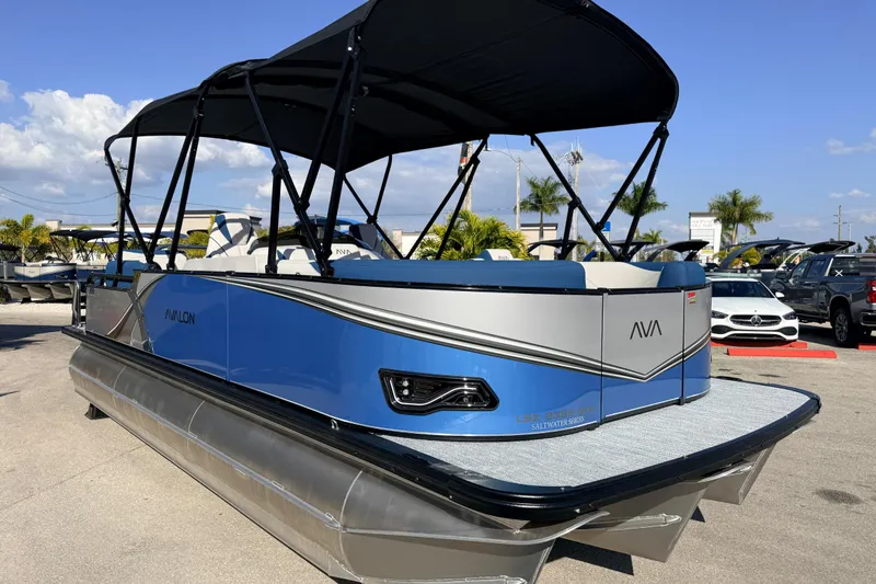 Slide: The Image of 2026 Avalon 2385 LSZ Quad Lounger Tri Toon boat, blue and silver, parked outdoors. - 6
