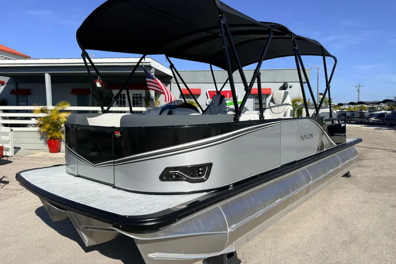 The Image of 2026 Avalon 2385 LSZ Quad Lounger Tri Toon boat with black canopy, parked outdoors. - 1