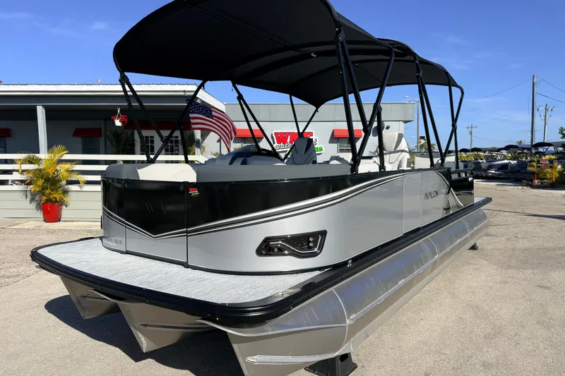Slide: The Image of 2026 Avalon 2385 LSZ Quad Lounger Tri Toon boat with canopy, parked outdoors. - 2