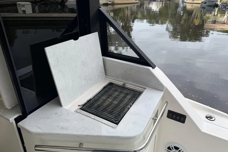 Slide: The Image of 2021 Regal 36 XO boat grill area with open cover, overlooking calm water. - 13