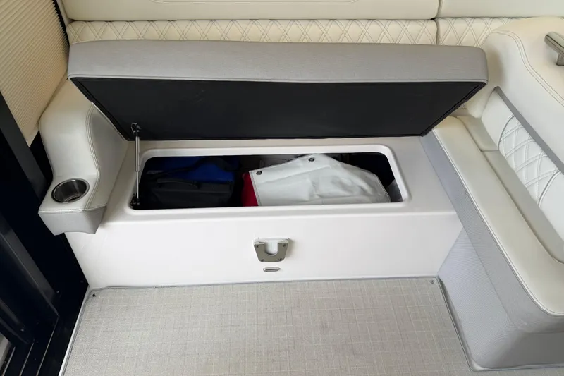 Slide: The Image of 2021 Regal 36 XO boat seat storage compartment with open lid, revealing interior items. - 27