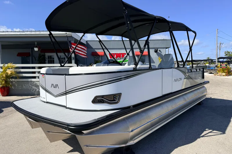 The Image of 2026 Avalon 2385 LSZ Versatile Rear Bench Tri Toon boat with canopy, parked outdoors. - 1