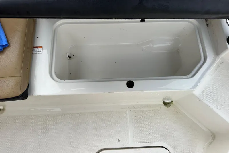 Slide: The Image of 2022 Sea Ray SPX 190 Outboard boat storage compartment, white interior, beige seat, blue cloth nearby. - 20