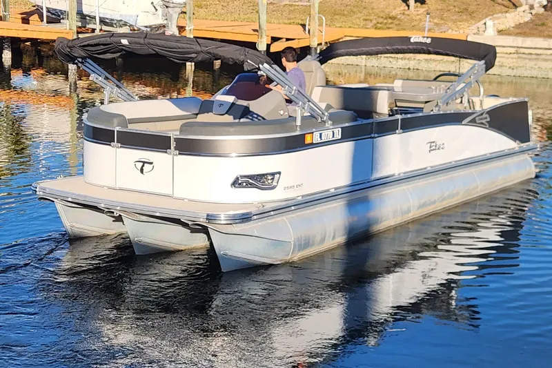 The Image of 2022 Tahoe Tritune 2585 ENT pontoon boat on calm water near a dock. - 0