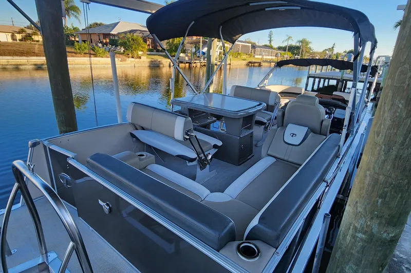 Slide: The Image of 2022 Tahoe Tritune 2585 ENT pontoon boat docked by a scenic waterfront. - 21