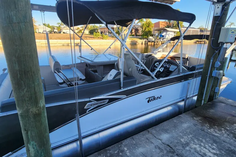 Slide: The Image of 2022 Tahoe Tritune 2585 ENT pontoon boat docked by a serene waterfront. - 22