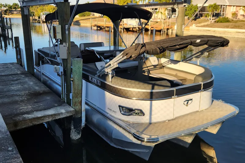 Slide: The Image of 2022 Tahoe Tritune 2585 ENT pontoon boat docked in a serene waterfront setting. - 24