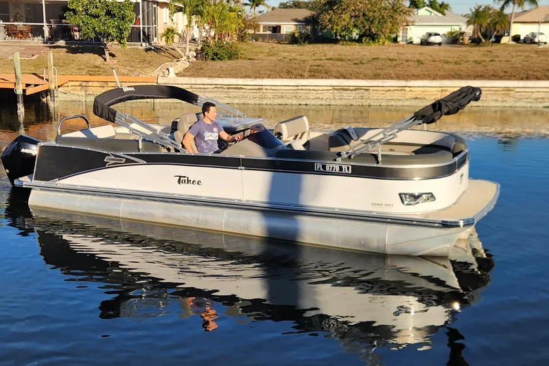 Slide: The Image of 2022 Tahoe Tritune 2585 ENT pontoon boat on calm water near residential area. - 3