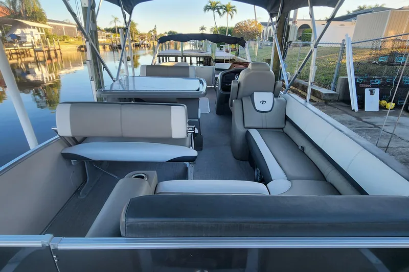 Slide: The Image of 2022 Tahoe Tritune 2585 ENT pontoon boat interior with seating and table, docked by a canal. - 42