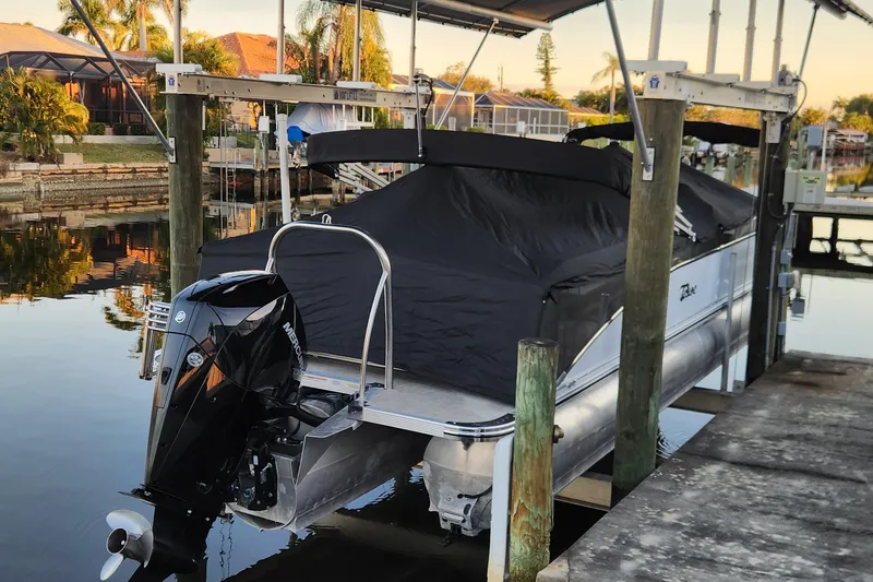 Slide: The Image of 2022 Tahoe Tritune 2585 ENT pontoon boat docked with cover, featuring Mercury outboard motor. - 46