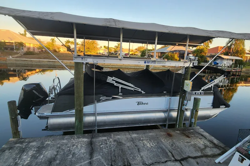 Slide: The Image of 2022 Tahoe Tritune 2585 ENT pontoon boat docked under a canopy on a calm waterway. - 47