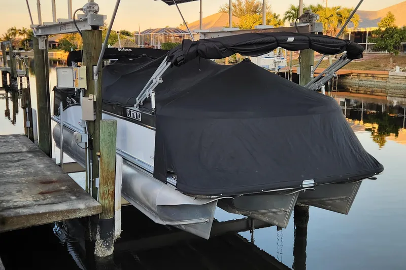 Slide: The Image of Covered 2022 Tahoe Tritune 2585 ENT pontoon boat docked on a lift. - 48