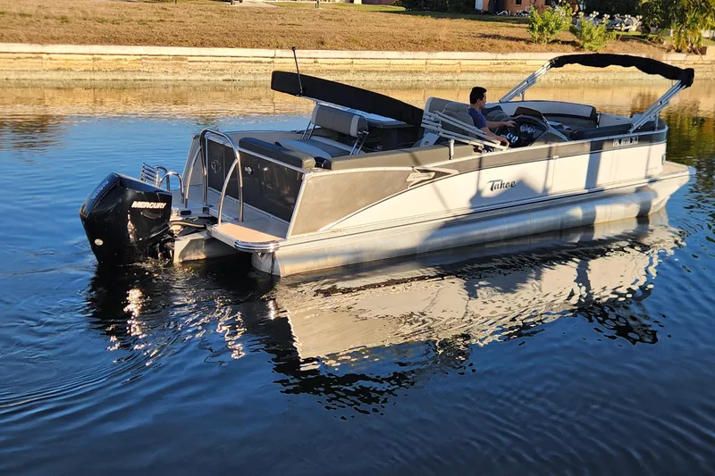 Slide: The Image of 2022 Tahoe Tritune 2585 ENT pontoon boat cruising on calm water. - 5