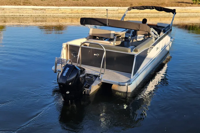 Slide: The Image of 2022 Tahoe Tritune 2585 ENT pontoon boat on calm water, rear view. - 9