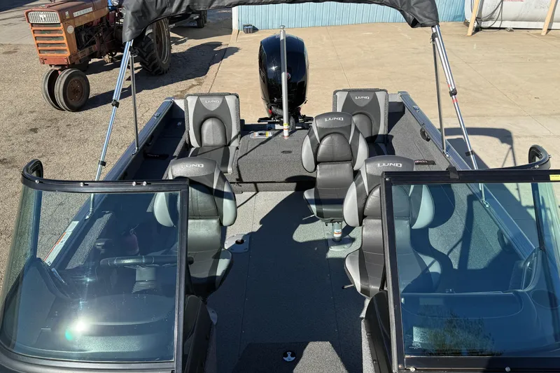 Slide: The Image of 2020 Lund 1875 Impact XS boat with seating and windshield, parked near a tractor. - 17