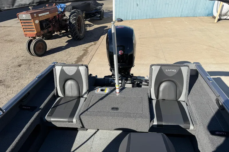 Slide: The Image of 2020 Lund 1875 Impact XS boat interior with seats and motor, parked near a vintage tractor. - 30