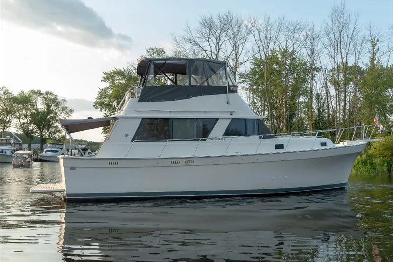 Slide: The Image of 1987 Mainship 36 Nantucket Sedan yacht on calm water, surrounded by trees. - 5