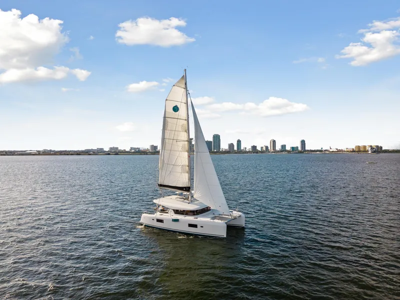 Slide: The Image of 2018 Lagoon 42 catamaran sailing on open water with city skyline in background. - 2