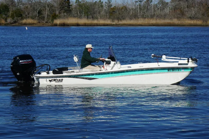 Slide: The Image of 2021 Mako Pro Skiff 17 CC boat on calm water, featuring a Mercury outboard motor. - 6