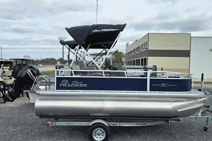 Slide: The Image of 2026 Sun Tracker Bass Buggy 16 XL Select pontoon boat on trailer, outdoor setting. - 13