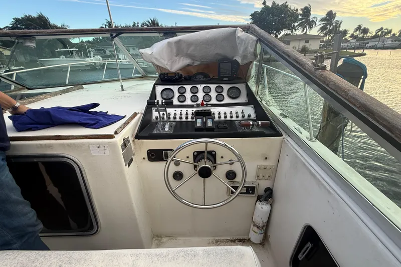 Slide: The Image of 1986 Chris-Craft 336 Commander helm with steering wheel and control panel, docked by water. - 11