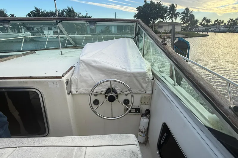 Slide: The Image of 1986 Chris-Craft 336 Commander boat helm with covered controls, docked by a scenic waterfront. - 9