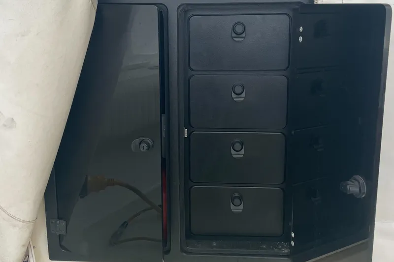 Slide: The Image of 2004 Carolina Classic 28 boat storage compartments with black drawers and electrical panel. - 26
