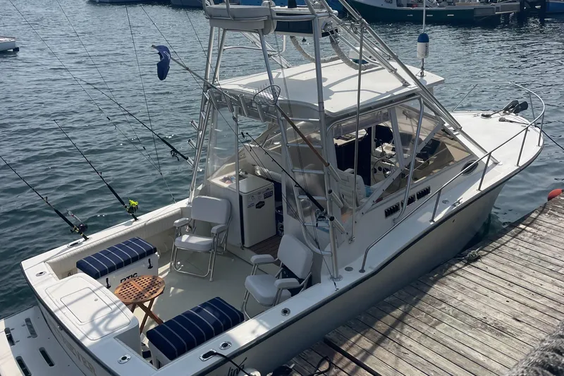 Slide: The Image of 2004 Carolina Classic 28 boat docked, featuring fishing rods and seating, on calm water. - 5