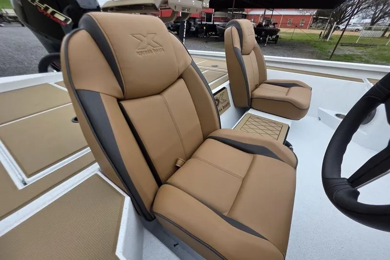 Slide: The Image of 2026 Xpress H20CC boat seats, tan and black, with steering wheel visible. - 19
