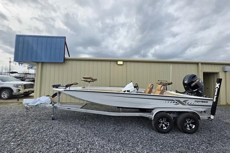 Slide: The Image of 2026 Xpress H20CC boat on trailer, parked outside a building under cloudy skies. - 2