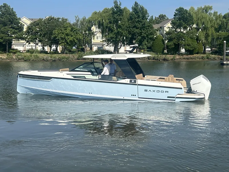 Slide: The Image of A modern Saxdor 320 GTO boat from 2027 on calm water, surrounded by trees and houses. - 4