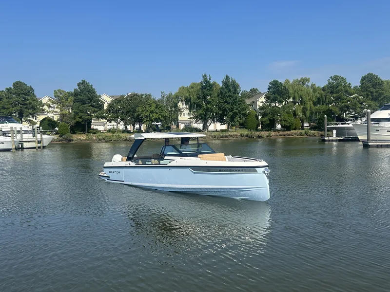 Slide: The Image of A 2027 Saxdor 320 GTO cruising on calm waters, surrounded by trees and houses. - 7