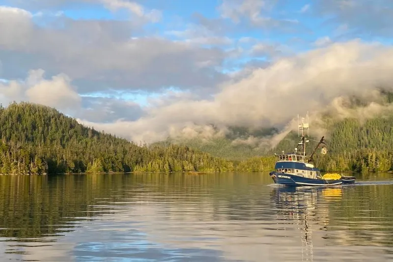 Slide: The Image of Custom 54 Steel Fishing Vessel (1976) on serene lake with forested hills and cloudy sky. - 5