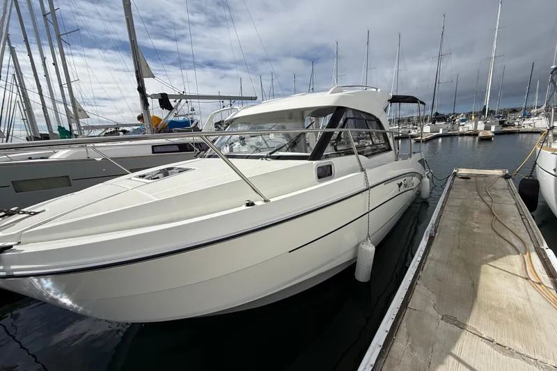 The Image of 2021 Beneteau Antares 8 docked at marina, surrounded by sailboats under cloudy sky. - 0