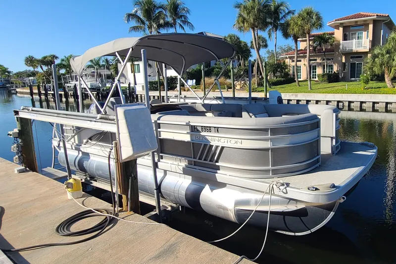 Slide: The Image of 2023 Bennington L23 pontoon boat docked by waterfront homes, under clear blue sky. - 1