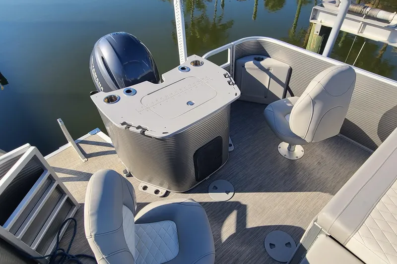 Slide: The Image of 2023 Bennington L23 pontoon boat interior with seating and motor, docked on calm water. - 12