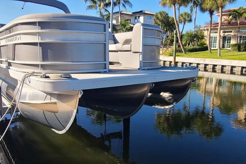 Slide: The Image of 2023 Bennington L23 pontoon boat docked on a calm waterway with palm trees. - 3
